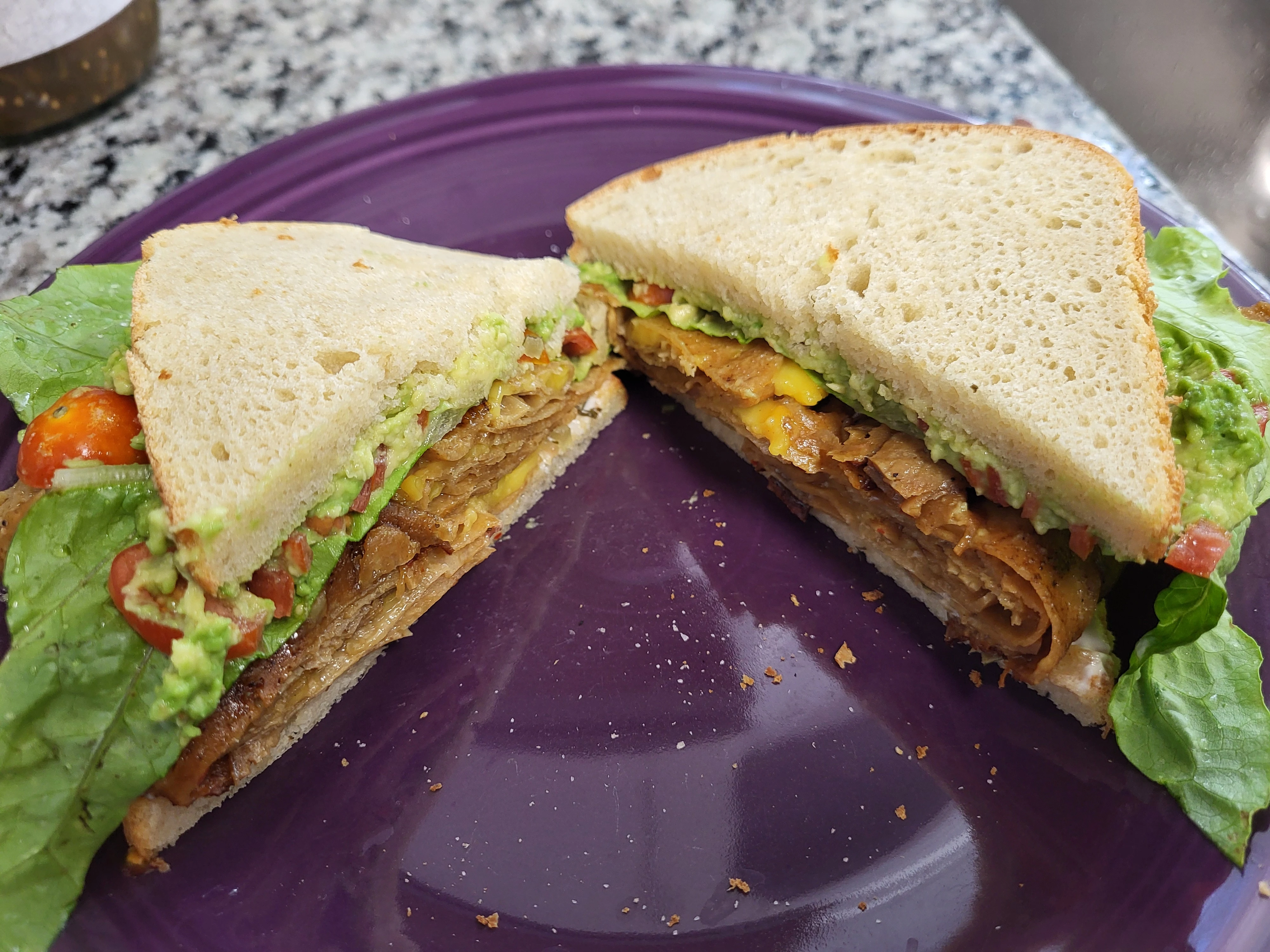 picture of sandwich with mashed avocado spread on white bread with lunch meat, cheese, tomato, and lettuce visible