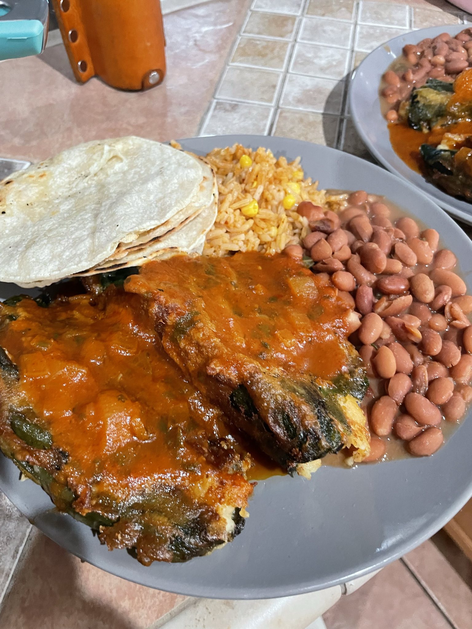 chile relleno, beans, rice and tortillas on a grey plate.